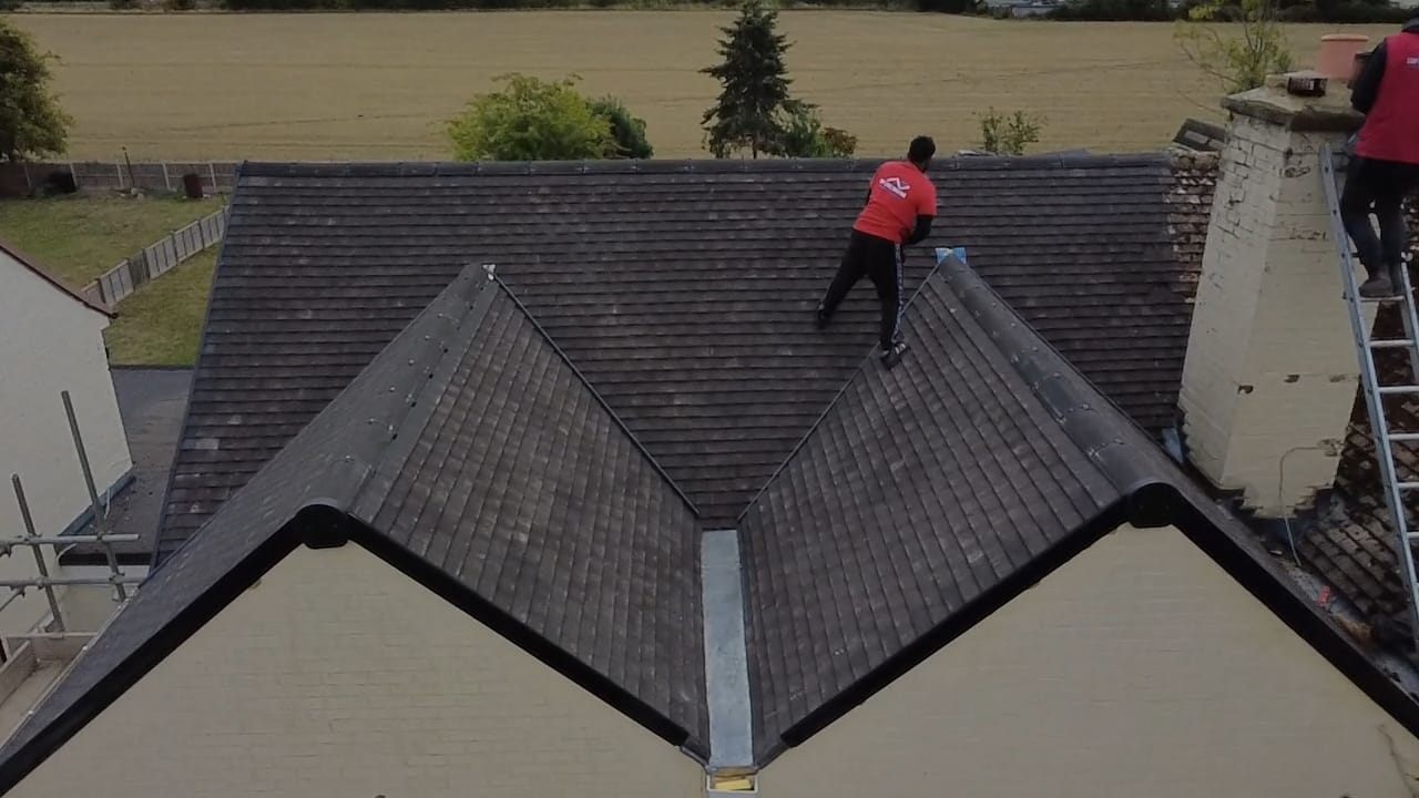 Aerial view of a finished dark tiled roof with a roofer on the ridge by Top Level Roofing & Building Solutions