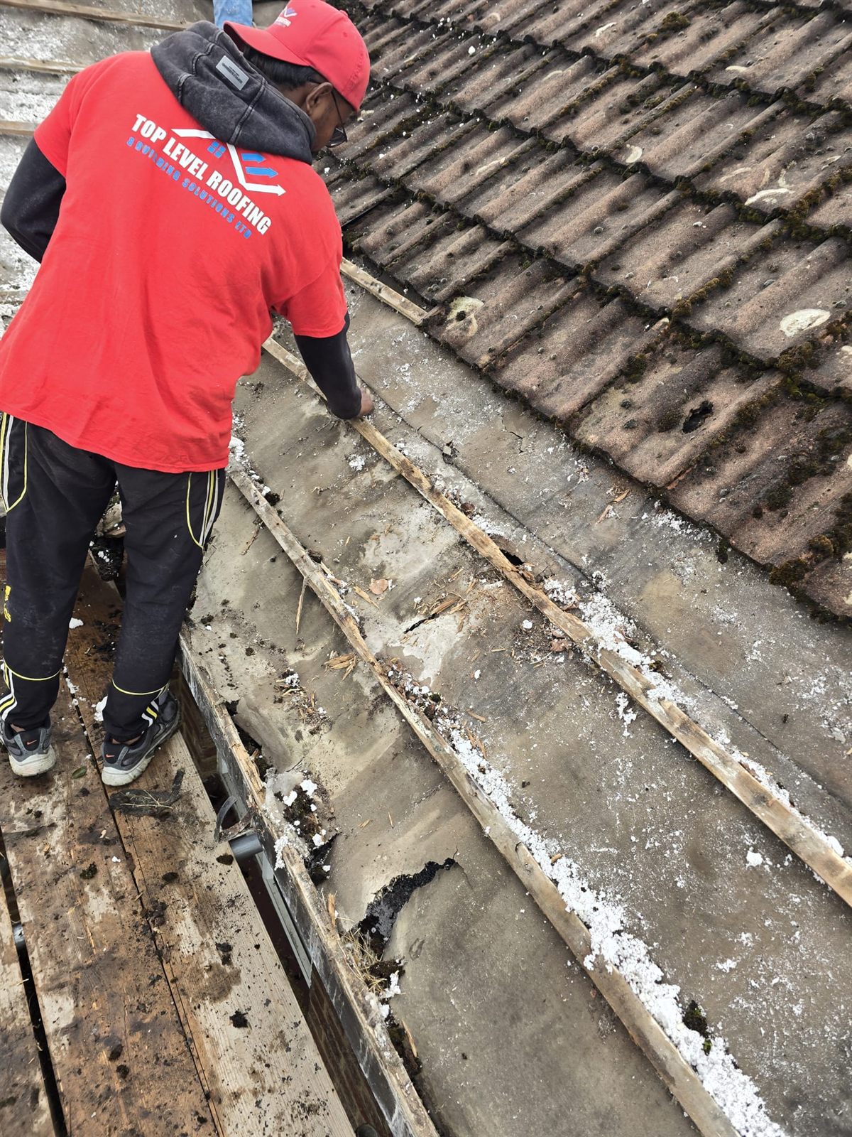 A Top Level Roofing roofer clearing debris from a lead valley gutter