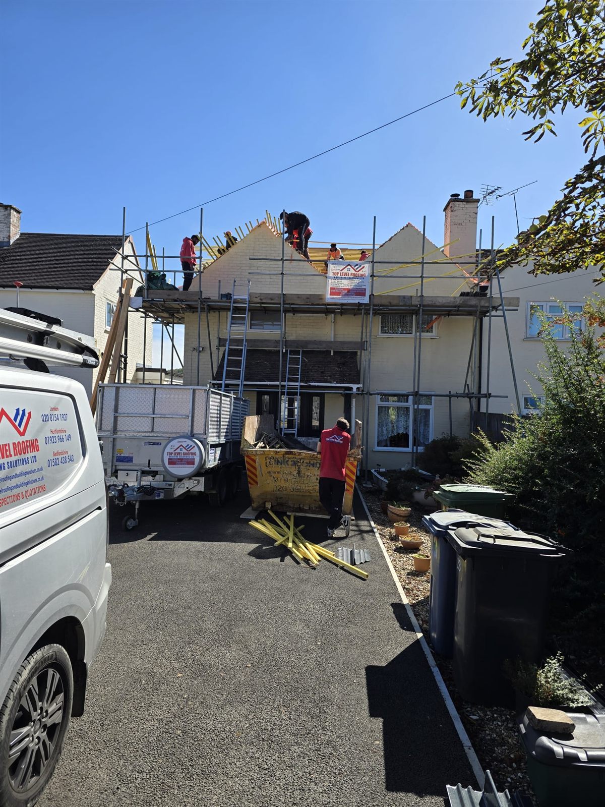 A branded Top Level Roofing van, trailer and team during a re-roof on a sunny day